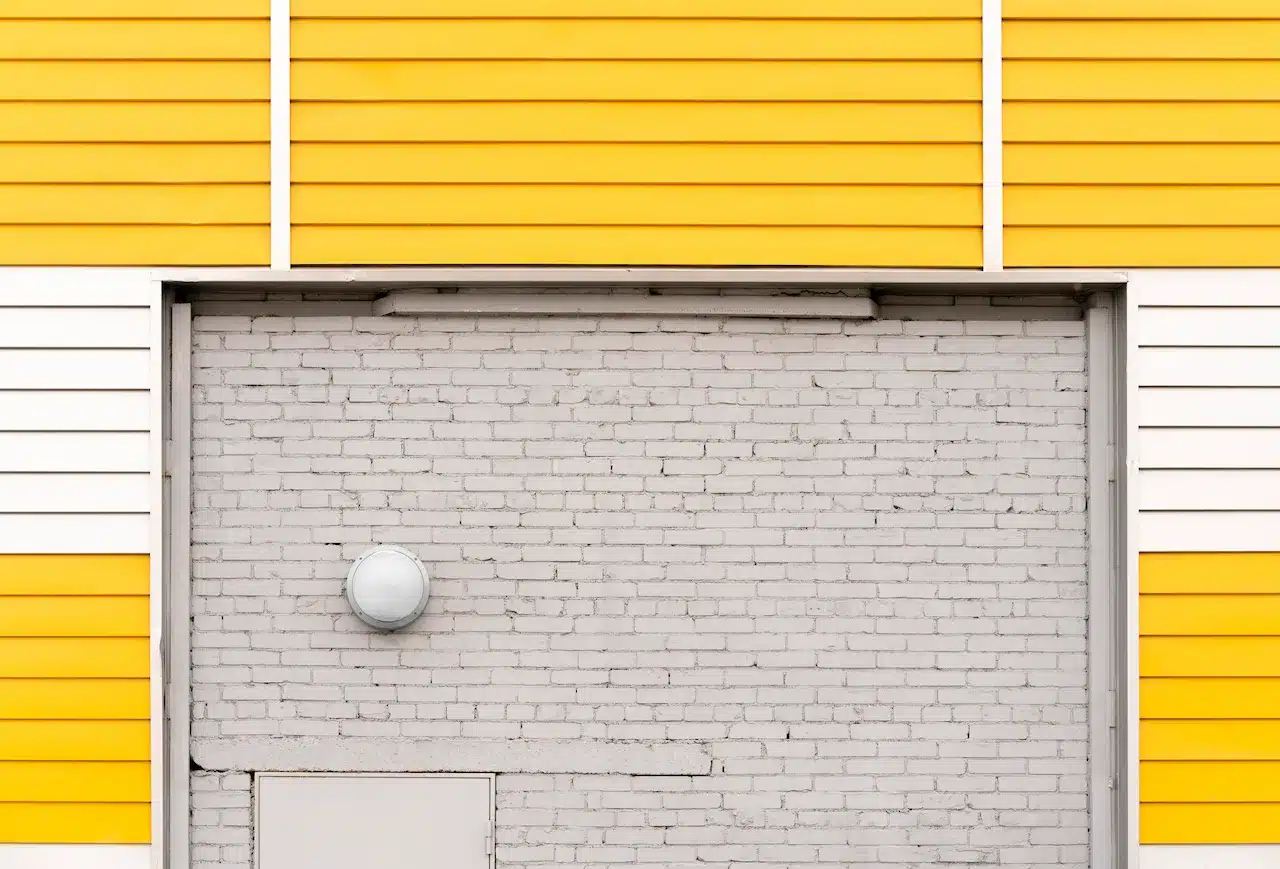 Yellow exterior wall with white brick surface, outdoor light fixture and small utility door on a building