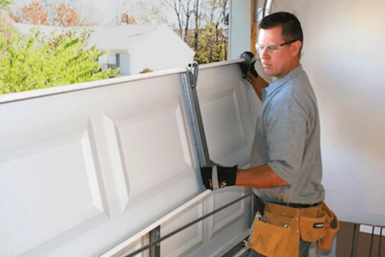 Garage door technician fixing a garage door track and mechanism during home maintenance repair.